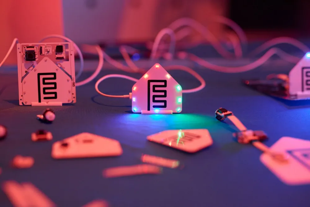 ESPHome Starter Kit modules on a table, with the ESPHome logo shaped notification module illuminated by rainbow LED lights.